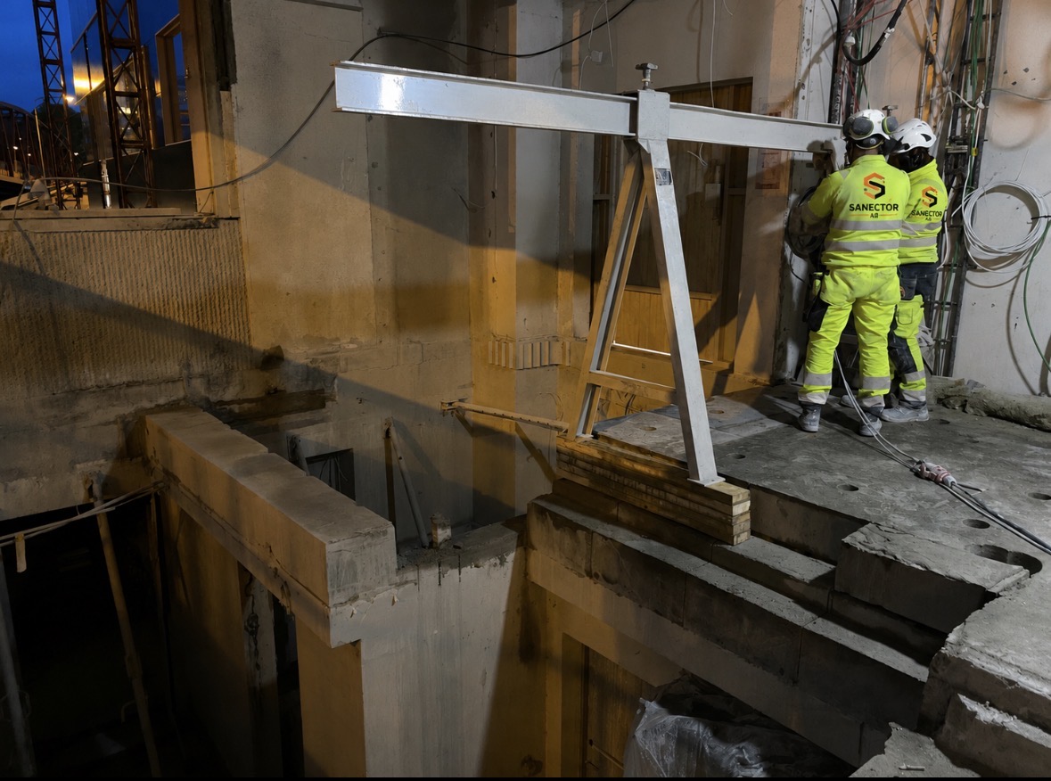 Sanektors personal utför bilningsarbete i ett schakt med lyftbalk under kvällstid i innerstadsmiljö