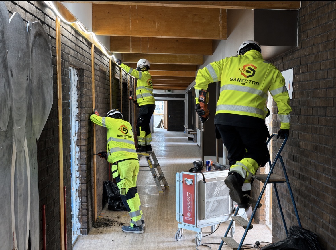 Tre saneringstekniker från Sanektor demonterar väggar och installationer i en korridor i en skola